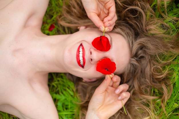 Uma jovem garota de cabelo comprido aprecia as cores da natureza em um campo de papoulas florescendo em um dia quente de verão.