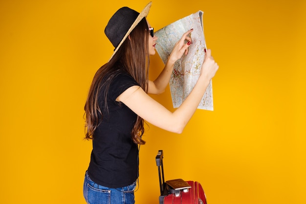 Uma jovem garota de cabelo comprido com um chapéu saiu em uma aventura, nas férias, olha para o mapa