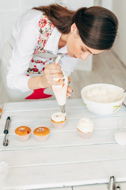 Uma jovem garota decora cupcakes com creme.