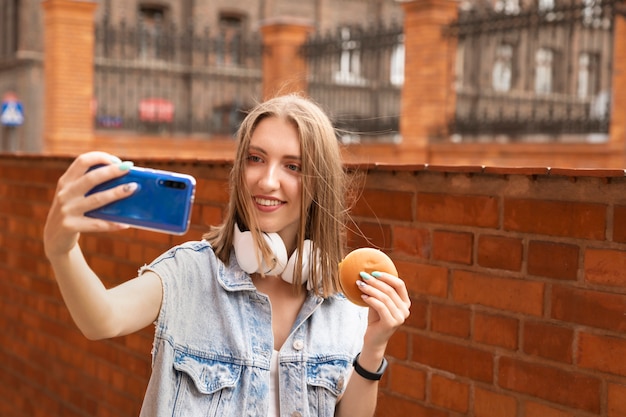 Uma jovem garota está comendo seu hambúrguer na rua. ela se diverte saboreando um delicioso lanche.