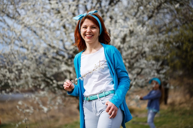 Uma jovem garota está em um jardim onde flores de cerejas e damascos. Ela está feliz respirando ar, flores primaveris ao fundo