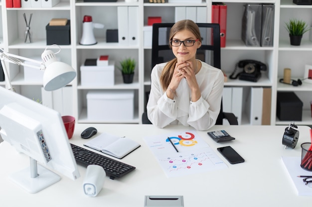 Uma jovem garota está sentada na mesa do computador no escritório.