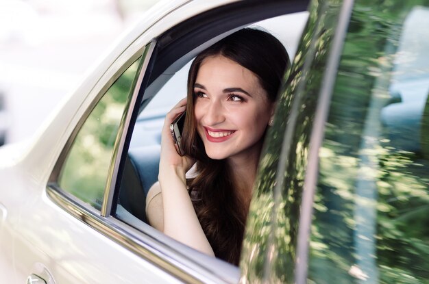 Uma jovem garota está sentada no banco de trás de um carro e está falando ao telefone.