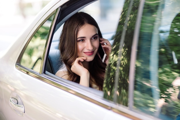 Uma jovem garota está sentada no banco de trás de um carro e está falando ao telefone.