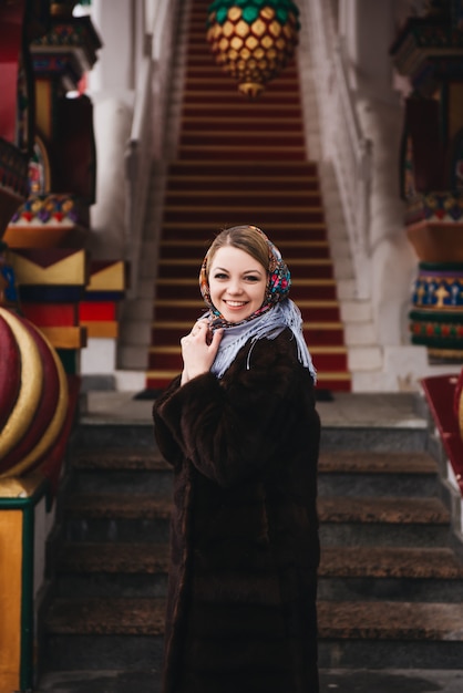 Uma jovem garota linda com um casaco de vison e um cachecol folclórico russo anda pelo kremlin de izmailovo. moscou, rússia.