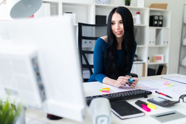 Uma jovem garota se senta no escritório à mesa e olha para o monitor.