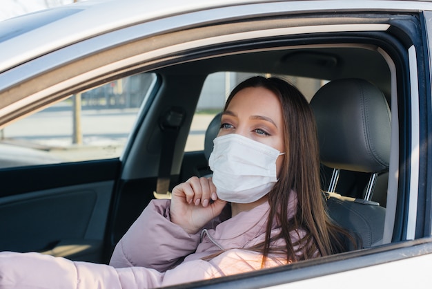 Uma jovem garota senta-se ao volante do carro na máscara durante a pandemia global e o coronavírus