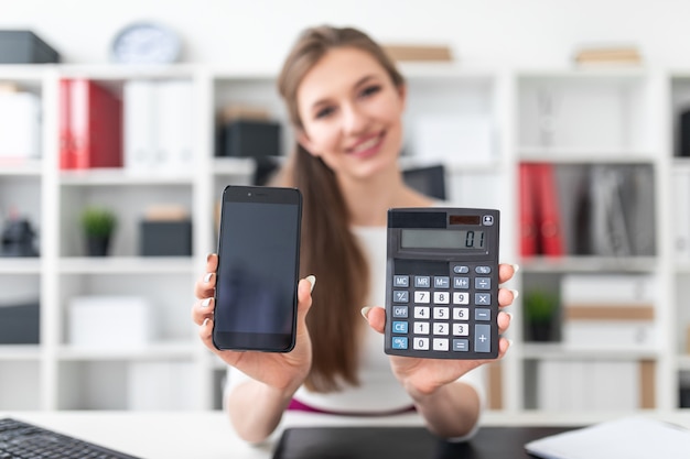 Uma jovem garota sentada em uma mesa e segurando um telefone e uma calculadora.