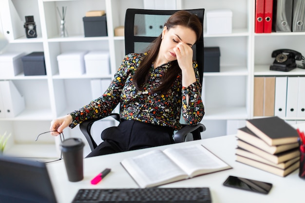 Foto uma jovem garota sentada no escritório à mesa do computador.