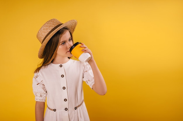 Uma jovem garota usando um chapéu de palha bebe café em um copo de papel