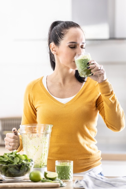 Uma jovem gosta de um smoothie de espinafre que ela mesma preparou Ela bebe uma bebida energética vegetal