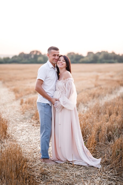 Uma jovem grávida com seu marido um lindo casal feliz abraçando em um campo dourado no campo Relações familiares Futuros pais