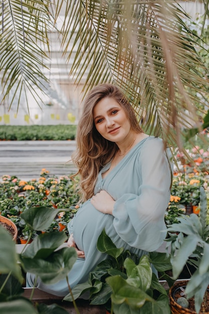 Uma jovem grávida está regando flores em uma estufa Primavera em casa e inverno fora da janela