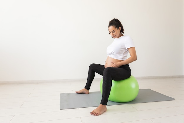 Uma jovem grávida fazendo exercícios de relaxamento com uma bola de fitness enquanto está sentada em um tapete