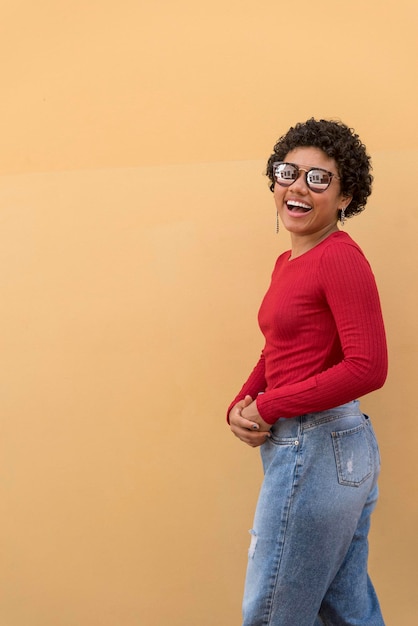 Uma jovem latina posando e sorrindo em frente a parede laranja com óculos de sol Panamá