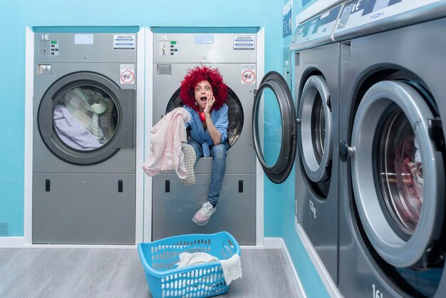 Uma jovem latina sorridente com cabelo afro sentado dentro de uma máquina de lavar em uma lavanderia automática azul