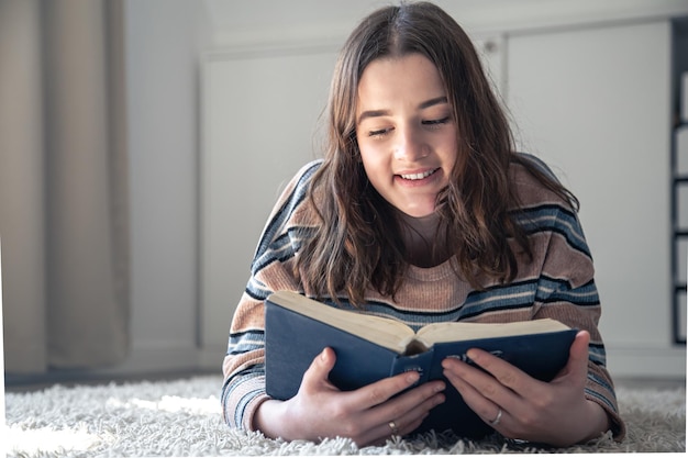 Uma jovem lendo um livro deitada no chão em casa