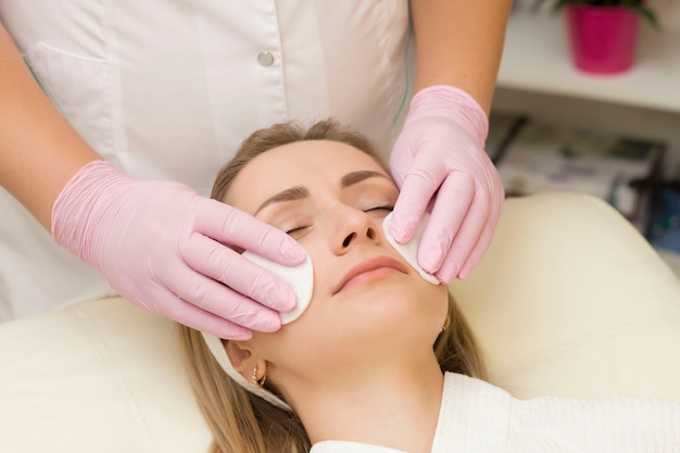 Uma jovem limpa o rosto com um cosmetologista de esponja. Procedimentos de spa. Relaxar