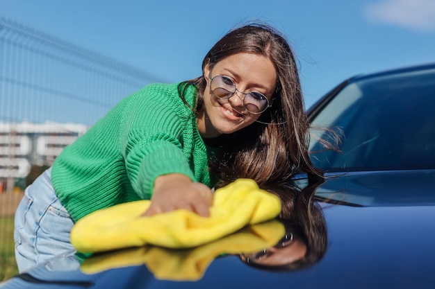 Uma jovem limpando e polindo seu carro com um pano de microfibra amarelo Conceito de cuidado do carro