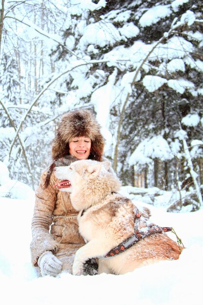 Uma jovem linda brinca com um cachorro husky em uma floresta de neve