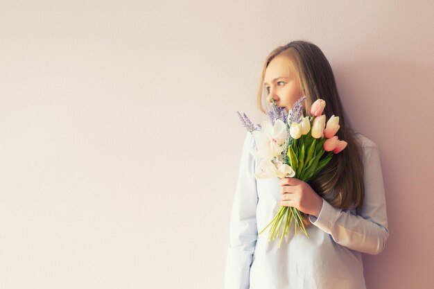 Uma jovem linda com cabelos longos loiros dissolvidos um chapéu de feltro na cabeça mantém flores da primavera