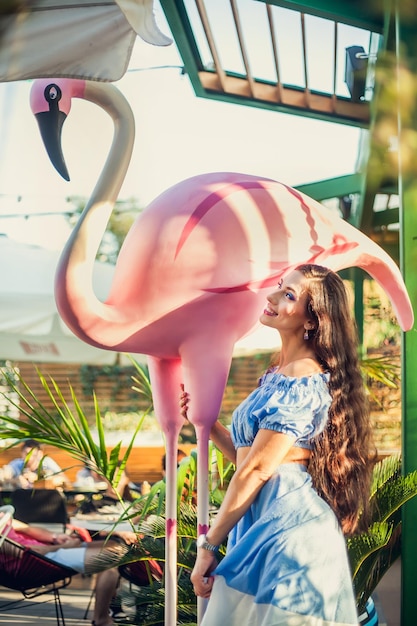 Foto uma jovem linda com longos cabelos escuros em um top curto fica ao lado de uma grande figura de flamingo e faz poses risos