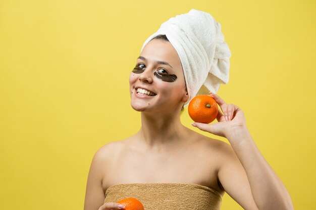 Uma jovem linda com uma toalha branca na cabeça usa adesivos de gel de colágeno sob os olhos