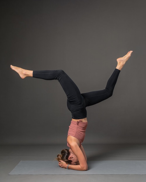 Uma jovem linda e magra está fazendo ioga em um fundo cinza Headstand