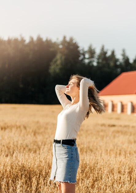 Uma jovem linda em uma saia jeans caminha por um campo de trigo em um dia ensolarado