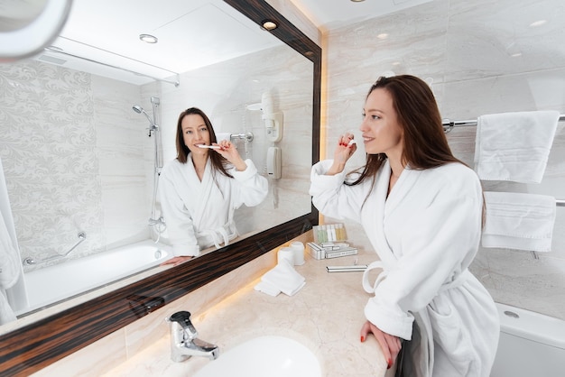 Uma jovem linda está escovando os dentes em um lindo banheiro branco Um bom dia fresco no hotel Descansar e viajar Recreação e turismo do hotel