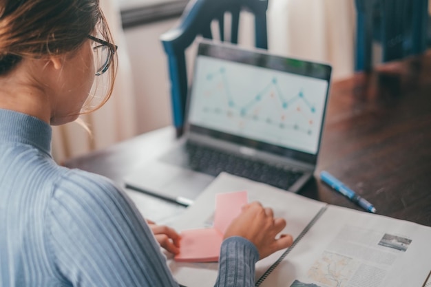 Foto uma jovem linda estudando e analisando gráficos no computador em casa adolescente feminino fazendo lição de casa na mesa com laptop usando internet