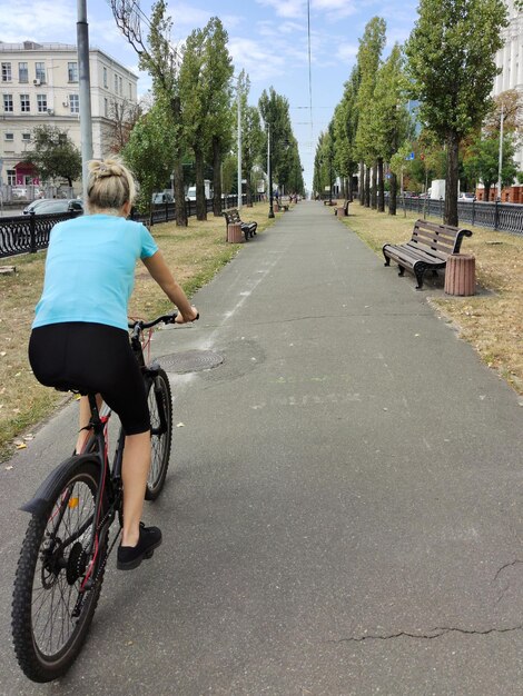 Uma jovem loira anda de bicicleta ao longo do beco em perspectiva Visão traseira Turismo e esportes