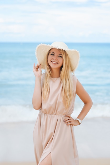 Uma jovem loira atraente com um chapéu e um vestido longo na praia