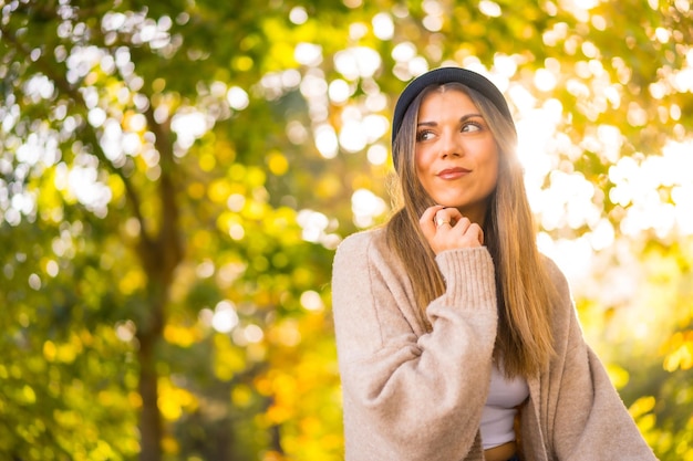 Uma jovem loira com um chapéu de lã no outono sentado no parque ao pôr do sol