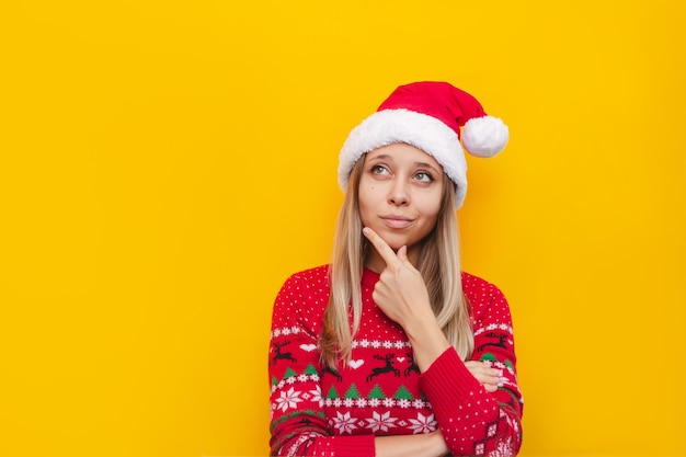 Uma jovem loira com um suéter de cervo vermelho e um chapéu de Papai Noel pensa olhando para o espaço da cópia