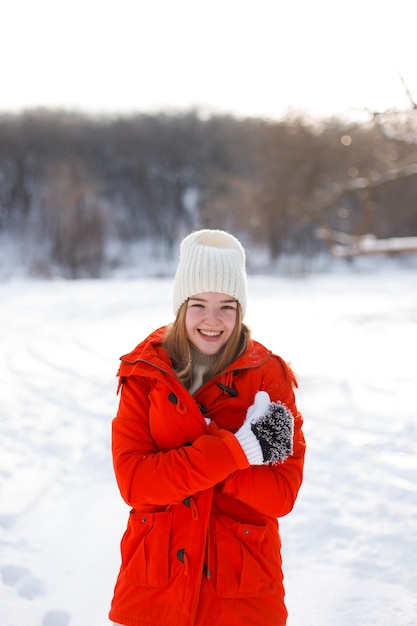 Uma jovem, loira, com um suéter, um chapéu e uma jaqueta laranja, tendo como pano de fundo a paisagem de inverno. Neve e geada, o conceito de Natal.