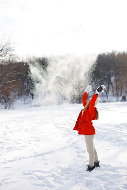 Uma jovem, loira, com um suéter, um chapéu e uma jaqueta laranja, tendo como pano de fundo a paisagem de inverno. Neve e geada, o conceito de Natal.