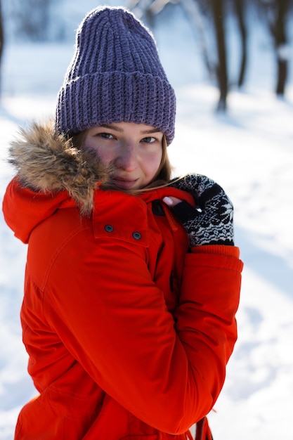 Uma jovem, loira, com um suéter, um chapéu e uma jaqueta laranja, tendo como pano de fundo a paisagem de inverno. Neve e geada, o conceito de Natal.