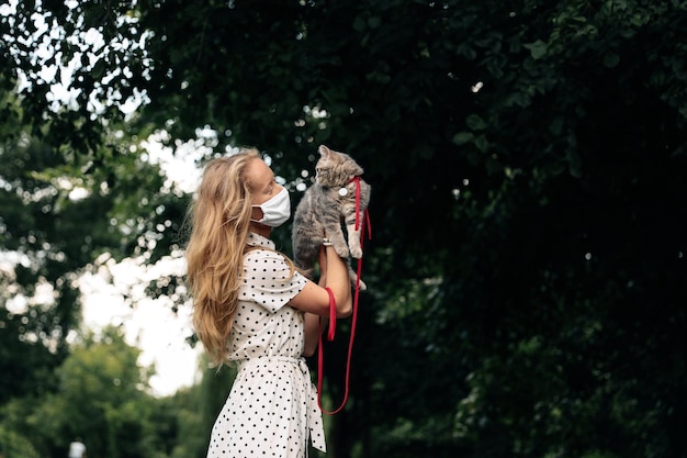 Uma jovem loira com uma máscara médica protetora segura um gatinho escocês de orelhas retas Uma garota caminha com um gato durante a pandemia de coronavírus kovid19 com medidas de segurança
