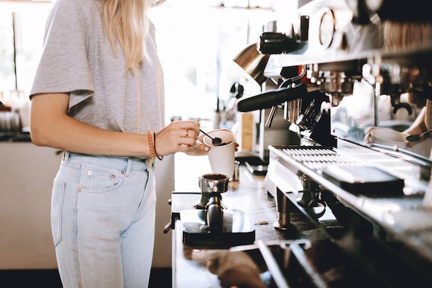 Foto uma jovem loira e magra, usando roupas casuais, está de pé ao lado da máquina de café em uma cafeteria aconchegante. .