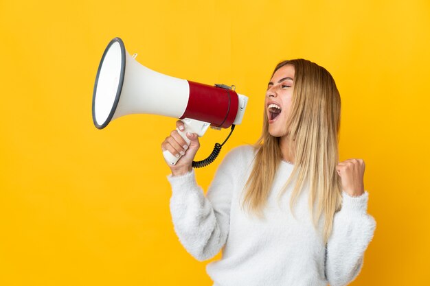 Uma jovem loira em uma parede isolada gritando em um megafone para anunciar algo em posição lateral