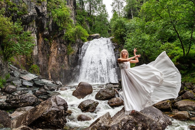 Foto uma jovem loira em uma pose elegante puxa um vestido boudoir nas montanhas contra uma cachoeira