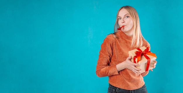 Uma jovem loira feliz usa jaqueta jeans verde, segura uma caixa de presente vermelha com laço de fita de presente