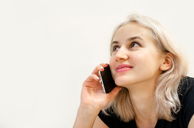 Foto uma jovem loira se comunica ao telefone. conversa feliz. comunicação virtual. sem sair de casa. fundo branco.