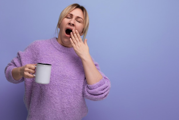 Uma jovem loira sonolenta do milênio em um visual casual revigora com uma xícara de café em um brilhante