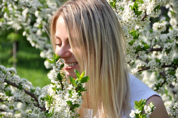 Uma jovem loira sorrindo e apreciando o cheiro de lilases brancos florescendo na primavera ao ar livre