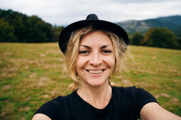 Foto uma jovem loira tira uma selfie com um chapéu preto e uma camiseta