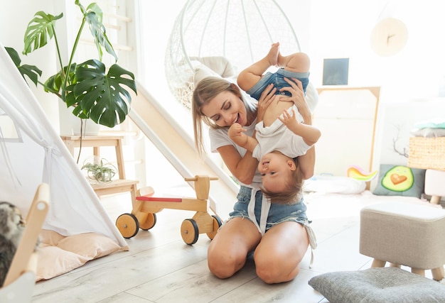 Uma jovem mãe bonita com a sua filhazinha estão a brincar na sala de brincadeiras com o cuidado e o amor maternos