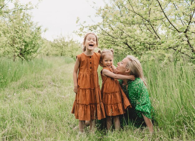 Uma jovem mãe brinca com duas filhas no jardim de primavera. crianças felizes e mãe