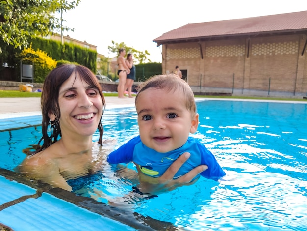 Uma jovem mãe caucasiana com seu bebê curtindo o verão nadando pela primeira vez em uma piscina